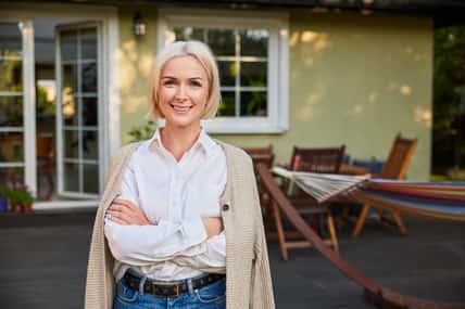 Portrait of happy mature woman standing outside her home backyard patio