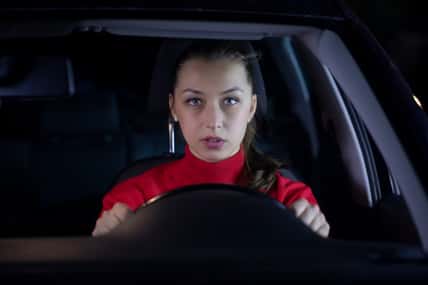 Woman is driving car at night. Serious female driver sitting inside car looks confused forward to the road clings tight to wheel on night trip. Concept: nerves and transportation. Safe journey