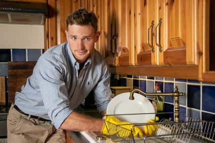 Good looking unhappy man washing plates and