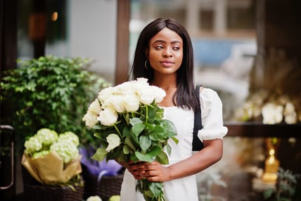 Beautiful african american girl holding bouquet of white roses flowers on dating in the city. Black businesswoman with bunch of flowers.