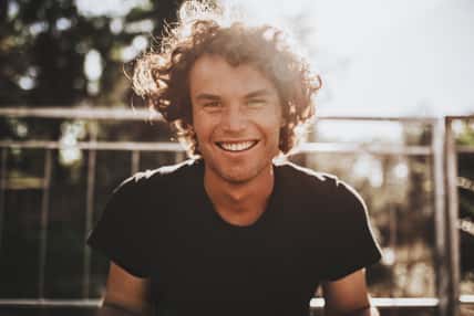 Outdoor closeup portrait of handsome freckled smiling male with curly hair, posing for social advertisement, in the city street on sunset sunlight with copy space for your promotional information