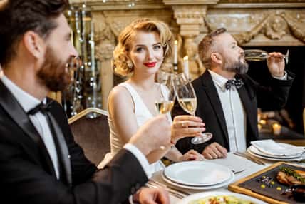 Elegantly dressed group of people having a festive dinner at a well-served table near the christmas tree, celebrating New Year holiday at the luxury restaurant