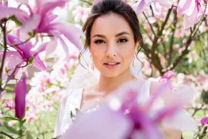Brunette bride looking at camera near blurred magnolia flowers