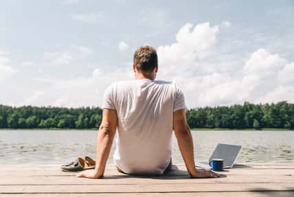 man sitting with laptop and looking on lake. working at vacation. summer time concept
