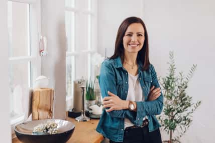 Relaxed smiling friendly woman with folded arms sitting perched on the edge of a table in her living room
