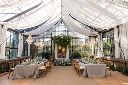 Wedding banquet hall in the greenhouse, tables are set, decorated with fresh flowers, candles, crystal chandeliers. Soft selective focus.