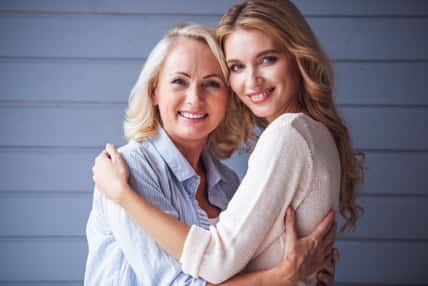 Beautiful senior mom and her adult daughter are hugging, looking at camera and smiling