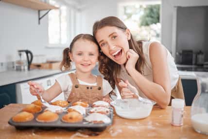 Baking, portrait and decorating with mother, daughter and learning cooking in home kitchen. Food, kids and help with girl and mom happy with muffins, cupcakes and icing results for bonding together.
