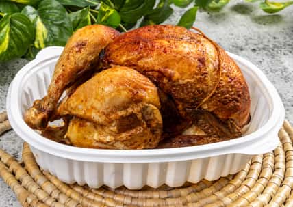 A whole rotisserie chicken in a take out pan