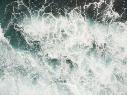 white sea foam on the ocean surface is agitated salt water from crashing waves and a strong surf, mixing currents and undertow swirl in the deep blue ocean during typhoon storms interrupt shipping