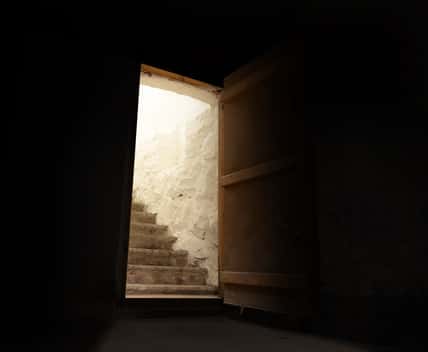 Open door in spooky dark basement with brightly lit stairs