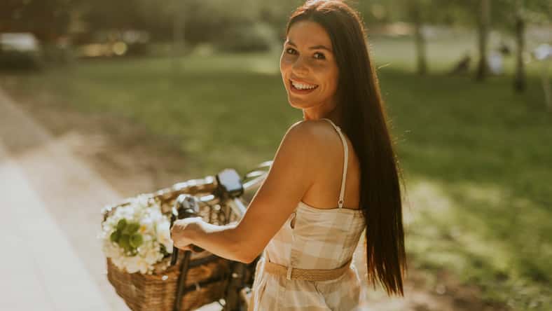 Pretty young woman with flowers in the basket of electric bike