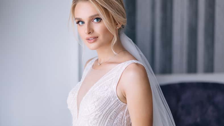 beautiful bride with blonde hair in elegant wedding dress posing in the room on wedding morning