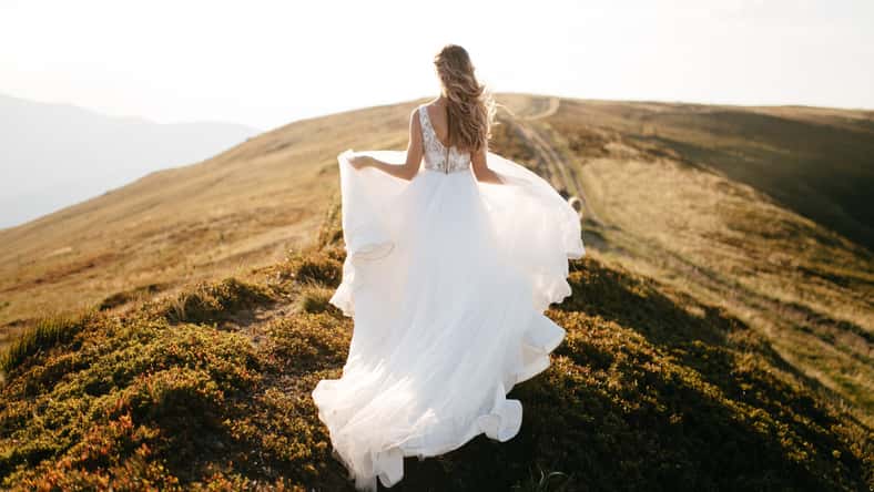 Stylish bride standing on beautiful landscape of mountains on sunset