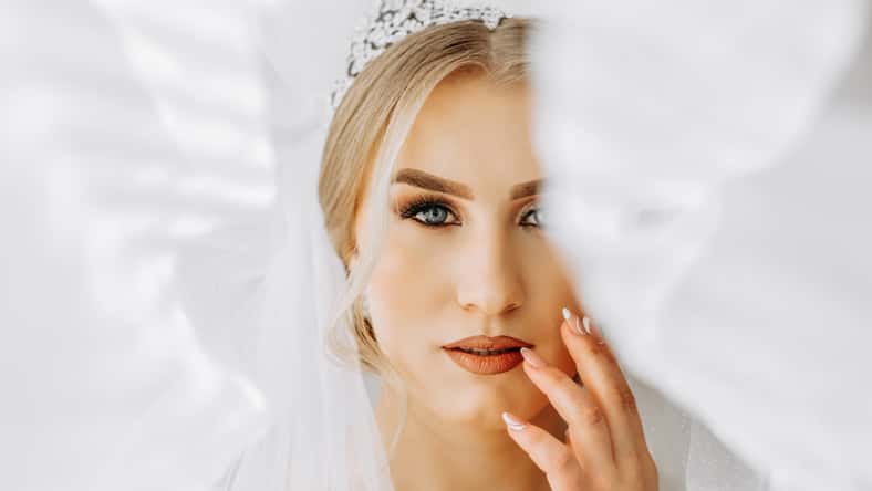 The bride in a white dress, veil poses in beautiful lighting in her room. Morning of the bride. A beautiful tiara