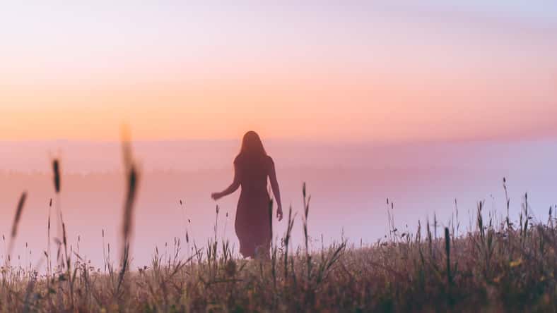 silhouette young woman in a dress walking on a hill on sunrise. female running on a foggy field and enjoying forest landscape. Active life, adventure, freedom, morning, nature concept. dew on grass.