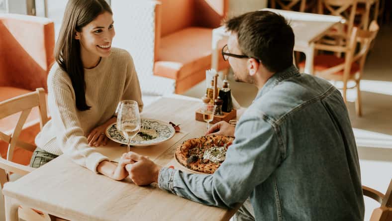 A couple enjoys a delightful evening, sharing dishes of flavorful cuisine and laughter while seated at a wooden table in a relaxed restaurant atmosphere.