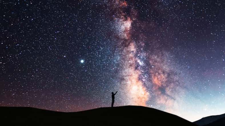 Beautiful starry sky with bright milky way galaxy. Night landscape . Person silhouette stands on the hill and looking at the starry sky.