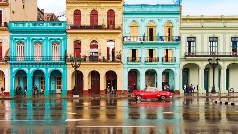 red classic car in front of colorful houses in old havana on a rainy day