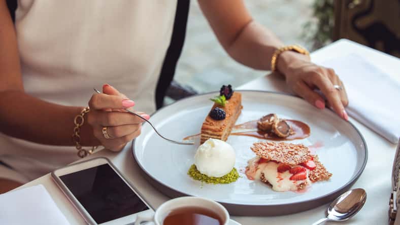 Tasting one cake from lots, close-up. Plate with different sweet desserts, hand taking one.
