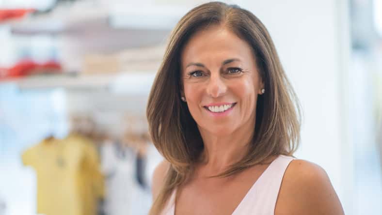Beautiful middle age hispanic woman standing with smile on face at clothes store. Shop owner and shop assistant smiling confident and cheerful