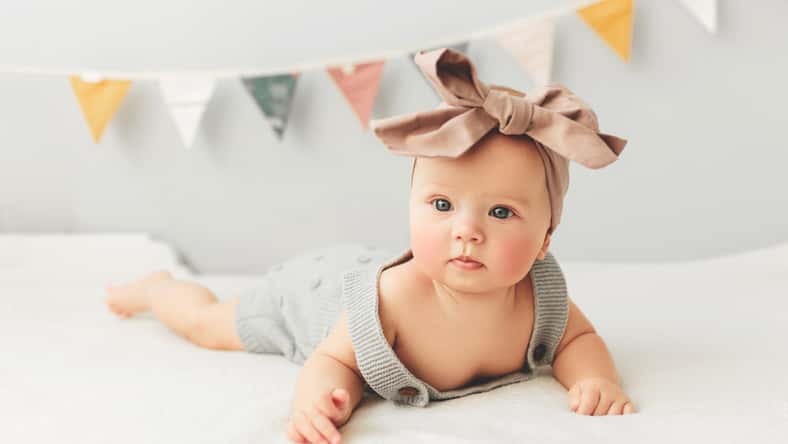 Beautiful baby lies on bed smiling bow on her head.