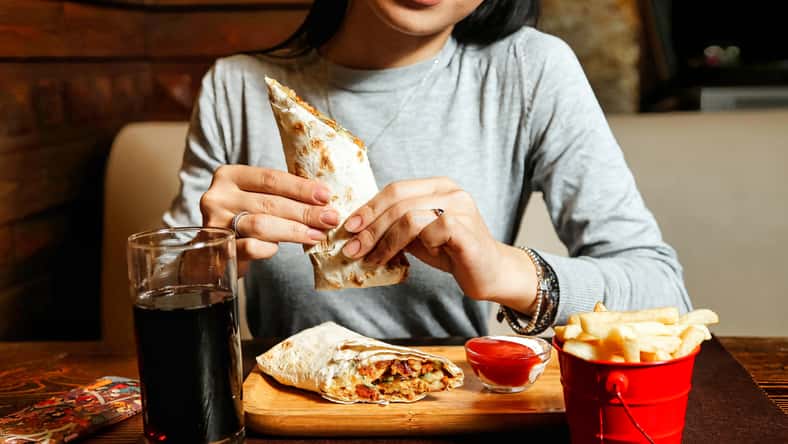 A woman is photographed seated at a table, enjoying a burrito.