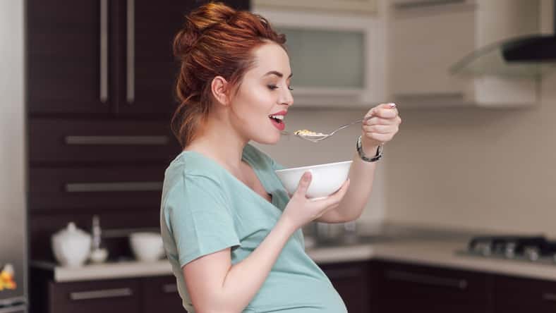 Beautiful pregnant woman eating with lust cereals on breakfast, enjoying meal. Yummy food for pregnant ladies