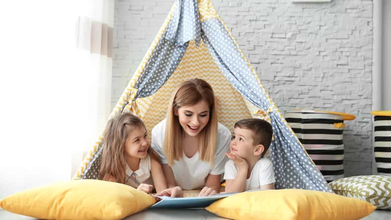 Nanny and little children reading book in