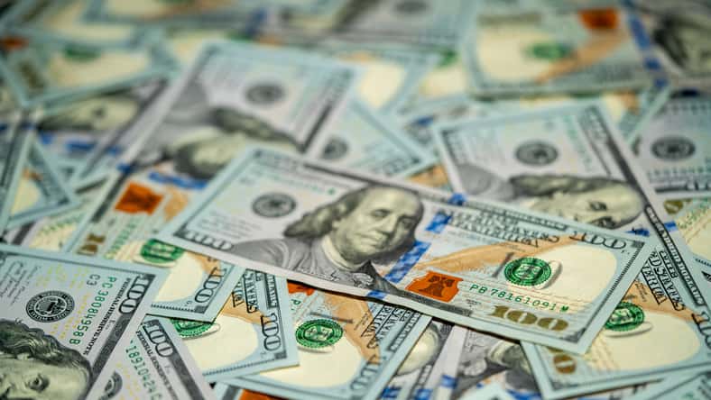 A collection of hundred dollar bills is spread out on a flat surface, showcasing the intricate designs and vibrant colors of the currency in detail.