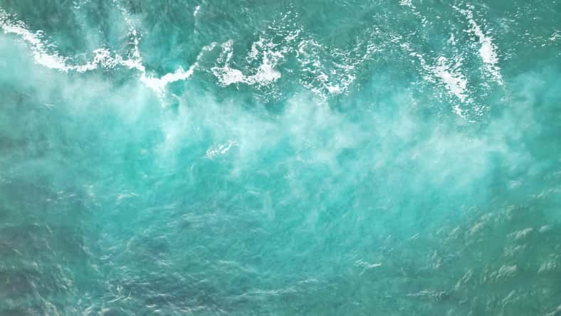Vista aérea de las ondas del océano turquesa con crestas blancas espumosas que crean un patrón abstracto fascinante en la superficie del agua.
