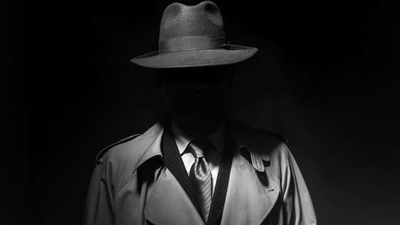 Man posing in the dark with a fedora hat and a trench coat, 1950s noir film style character