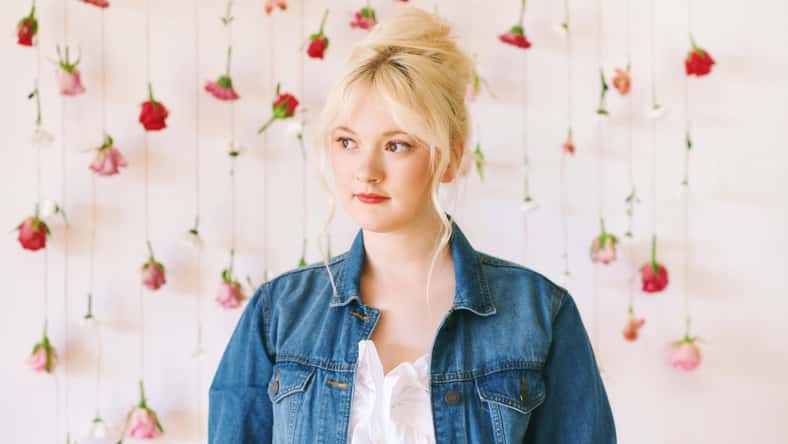Studio portrait of pretty young teenage 15 - 16 year old girl wearing denim jacket, posing on white background with hanging flowers, beauty and fashion concept