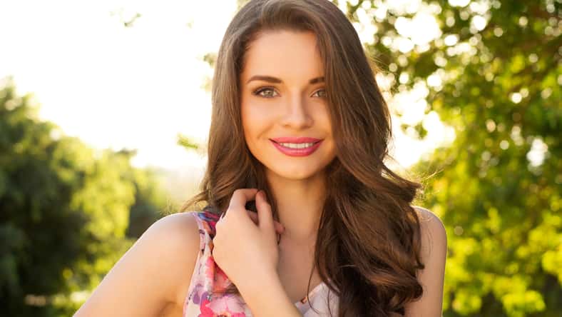 Hermosa chica sonriente que te mira contra el fondo de la primavera verde bokeh