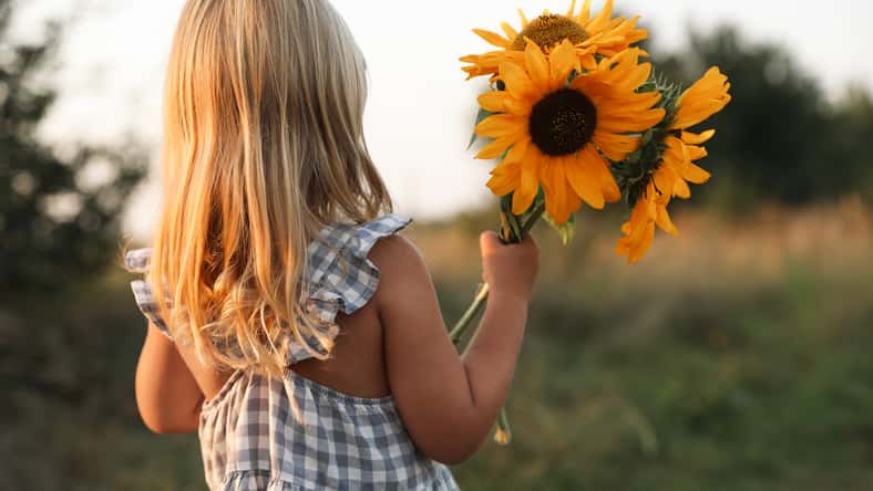 Little girl with sunflowers at meadow, back view. Child enjoying beautiful nature