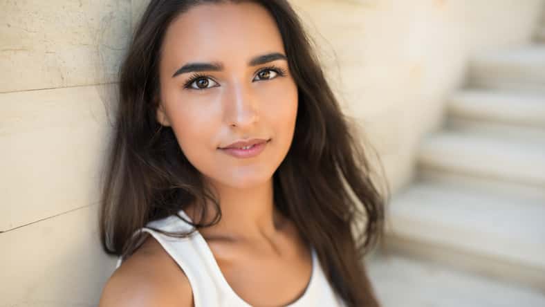 Close-up portrait of beautiful young brunette woman, smiling and sitting on steps of a park.