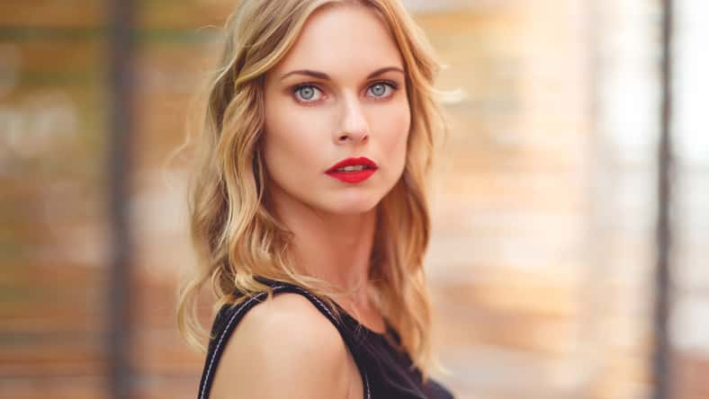 Closeup portrait of beautiful girl with curly blond hair and red lipstick on blurred background