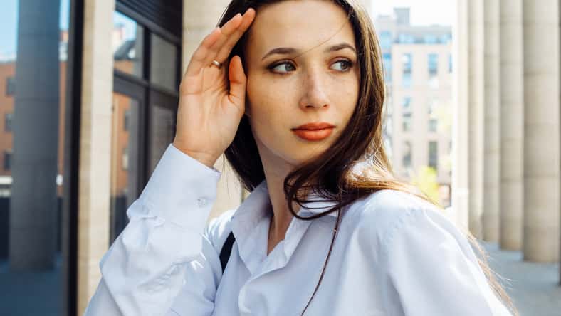 Fashionable brunette woman in the city. Young female model with long hair wears white shirt.