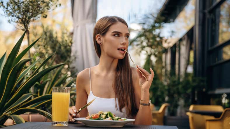 Delicious food. Beautiful young woman is outdoors of the restaurant by the table.