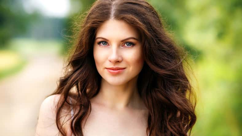 Beautiful young woman close-up in white dress, against green of park.