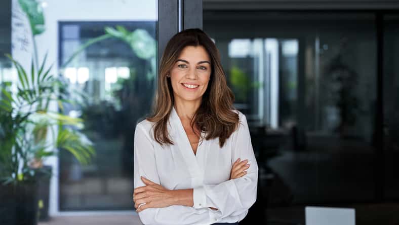 Happy elegant older mature lady posing for portrait standing in office. Beautiful middle aged business woman looking at camera, smiling 45 years old businesswoman leader executive at work.