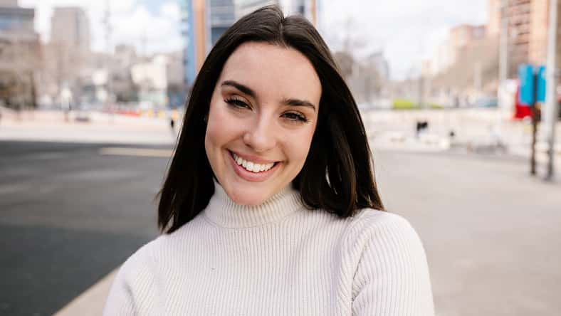 Portrait of young happy pretty woman smile at camera outside. Millennial cheerful girl showing toothy smile standing at city street