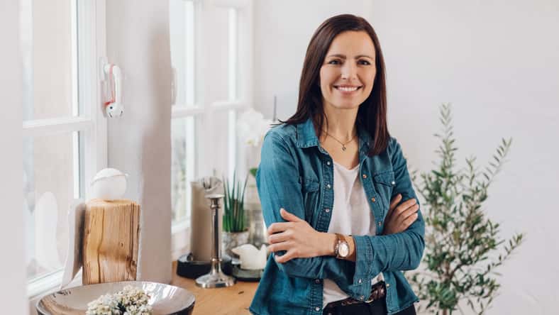 Relaxed smiling friendly woman with folded arms sitting perched on the edge of a table in her living room