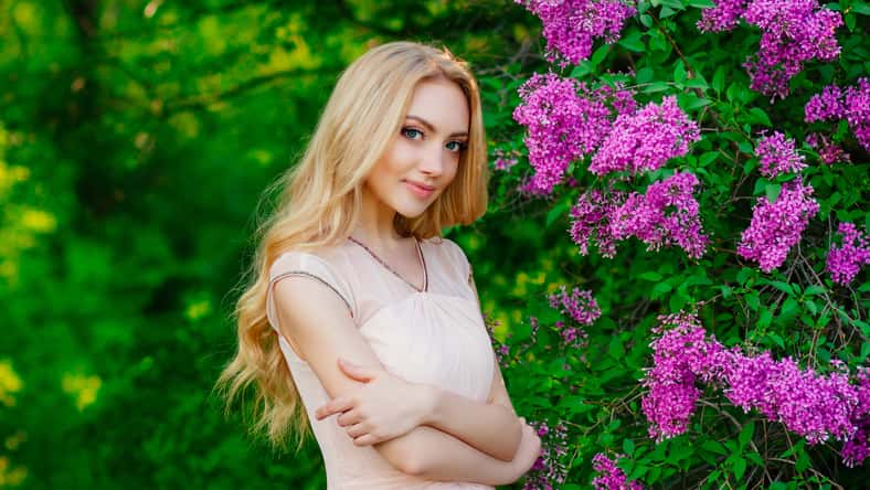 charming beautiful blonde girl, portrait of girl surrounded by blooming flowers , beautiful smile, girl in spring garden