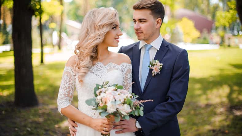 Portrait of a young bridegroom embracing a lovely blonde bride holding a beautiful bouquet of flowers