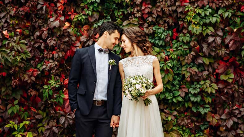 groom and bride posing in front of old brick wall with ivy