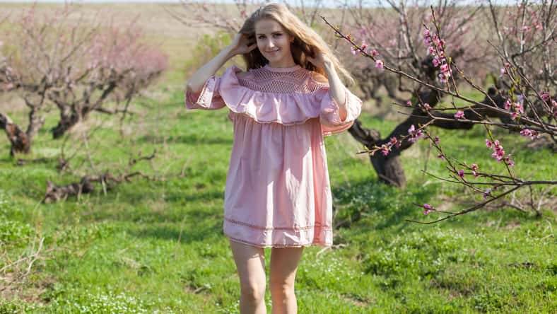 blonde girl walks through the garden blossoming peach