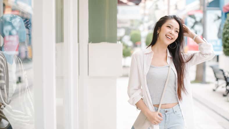 Summer sunny lifestyle fashion portrait of young stylish hipster Asia woman walking on the street, wearing cute trendy outfit