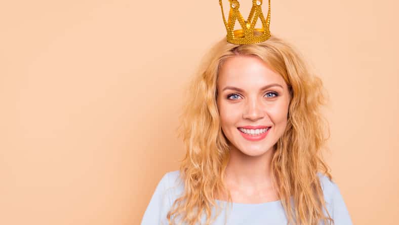 Portrait of attractive beautiful curly-haired cheerful blonde caucasian young girl wearing golden crown on head. Copy space. Isolated over grey background