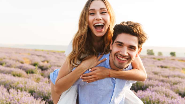 Cheery young couple having fun at the lavender field together, piggyback ride